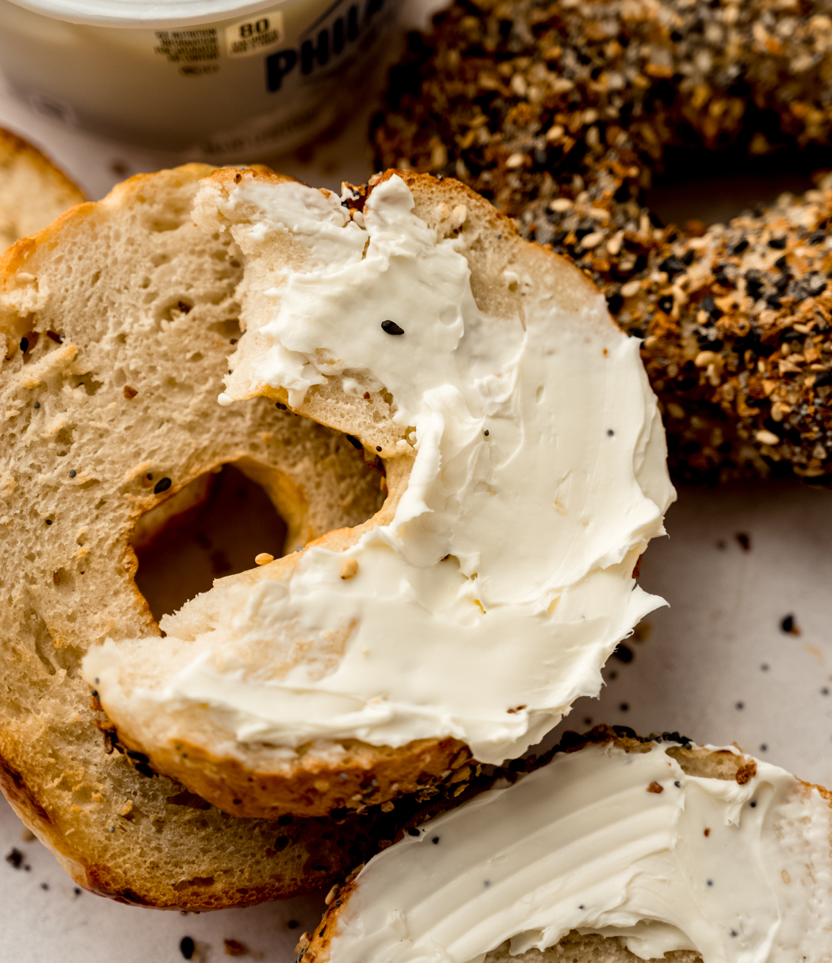 Aerial photo of homemade bagels and one has been split and spread with cream cheese.
