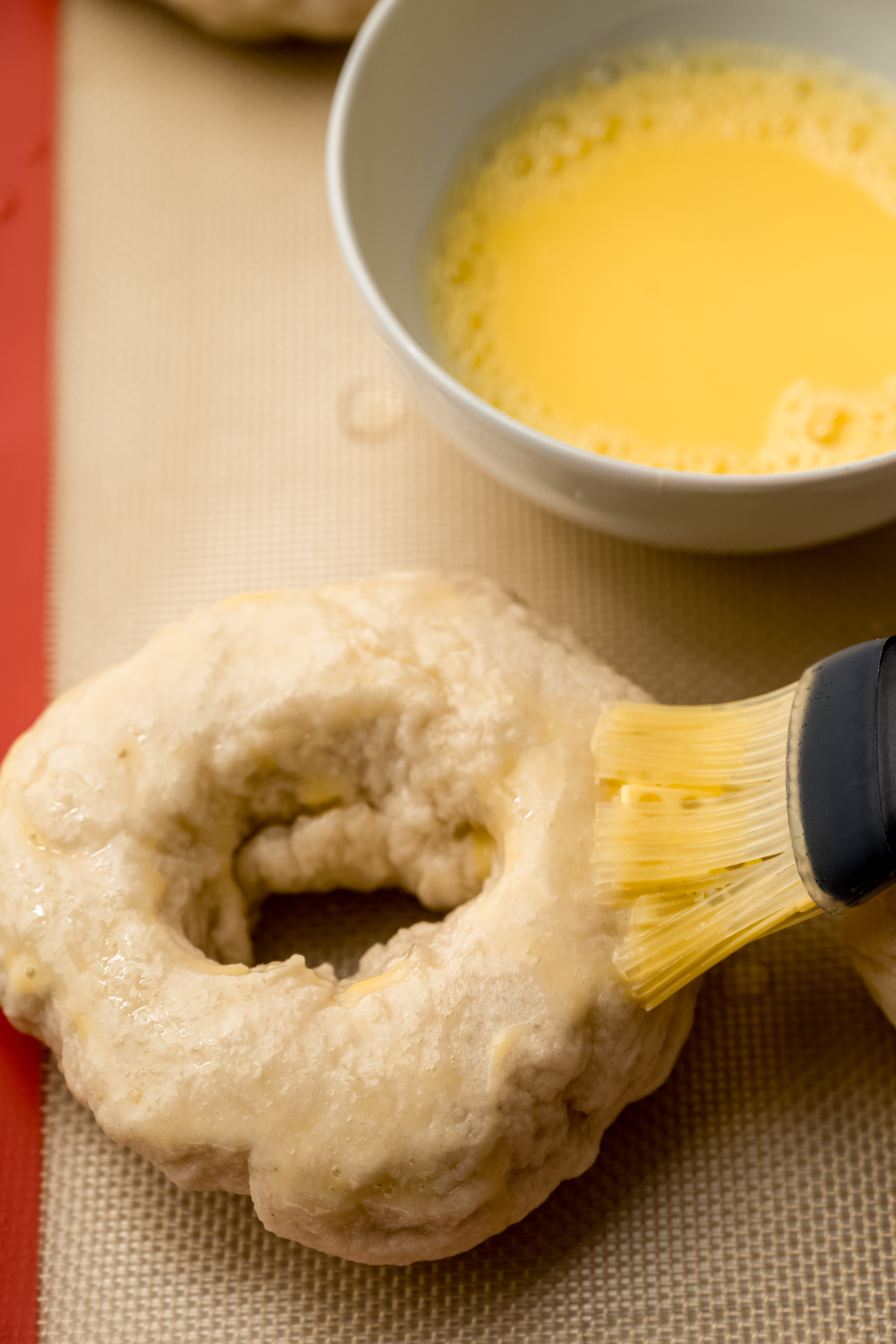 Someone is using a pastry brush to brush an egg wash on homemade bagels.