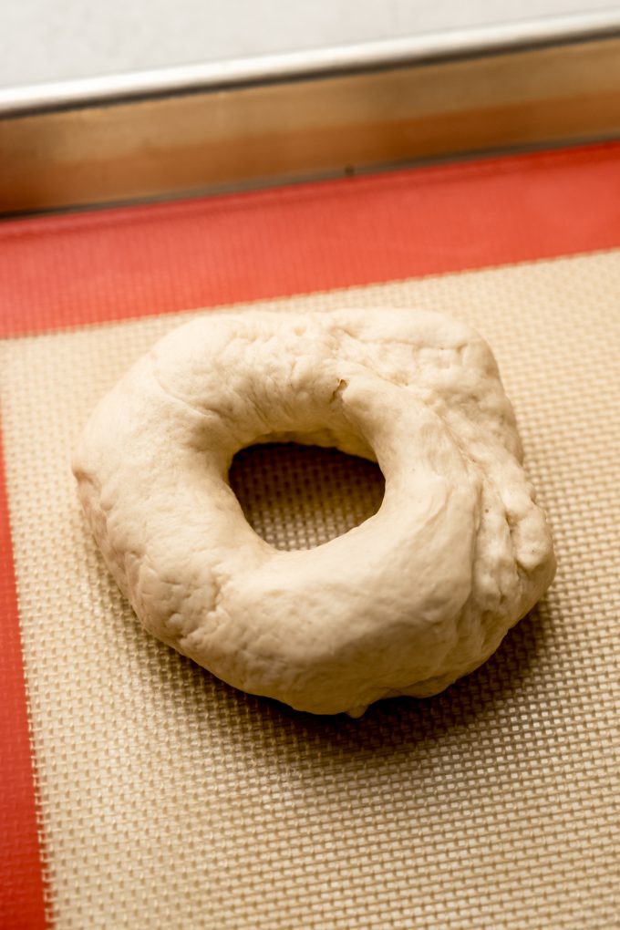 A ring of homemade bagel dough on a baking sheet.