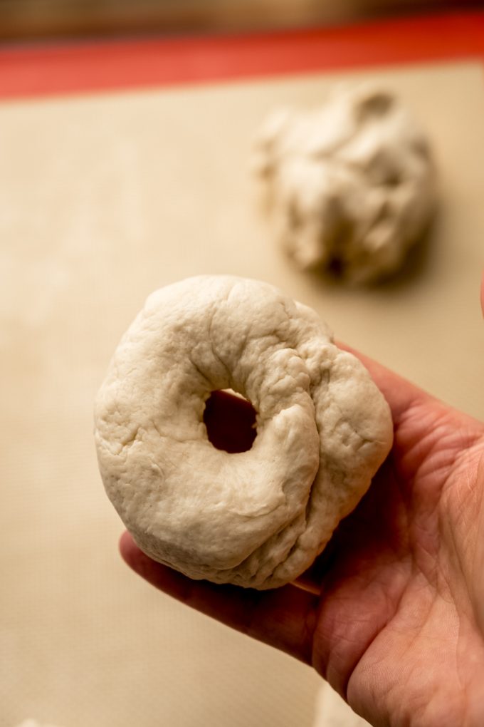 Someone is holding a ring of dough to make bagels.
