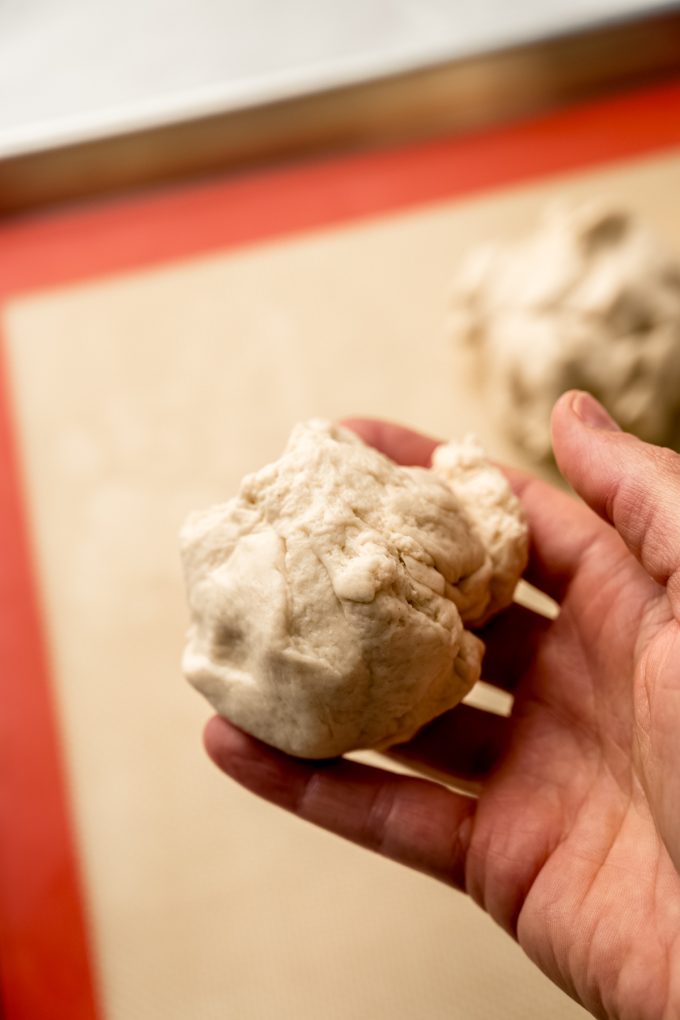 Someone is holding ball of dough to make bagels.