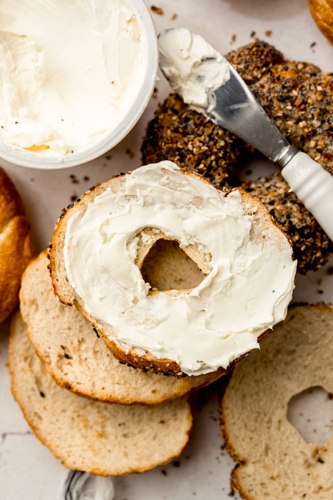 Aerial photo of homemade bagels and one has been split and spread with cream cheese.