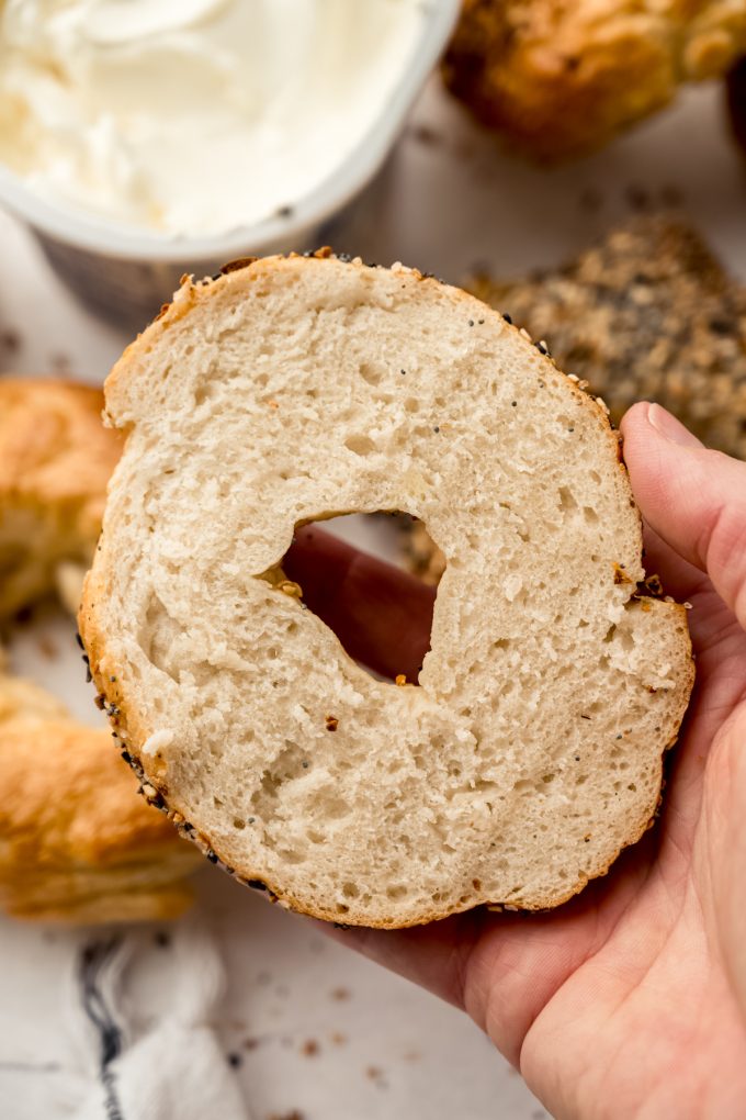 Someone is holding half of a sliced bagel in their hand.