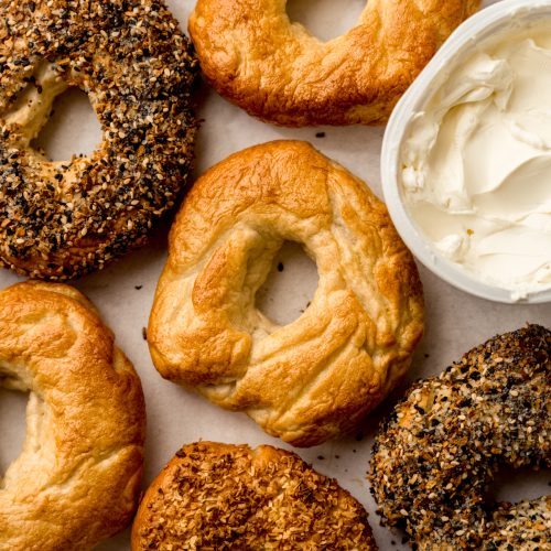 Aerial photo of homemade bagels on a surface with a tub of cream cheese.