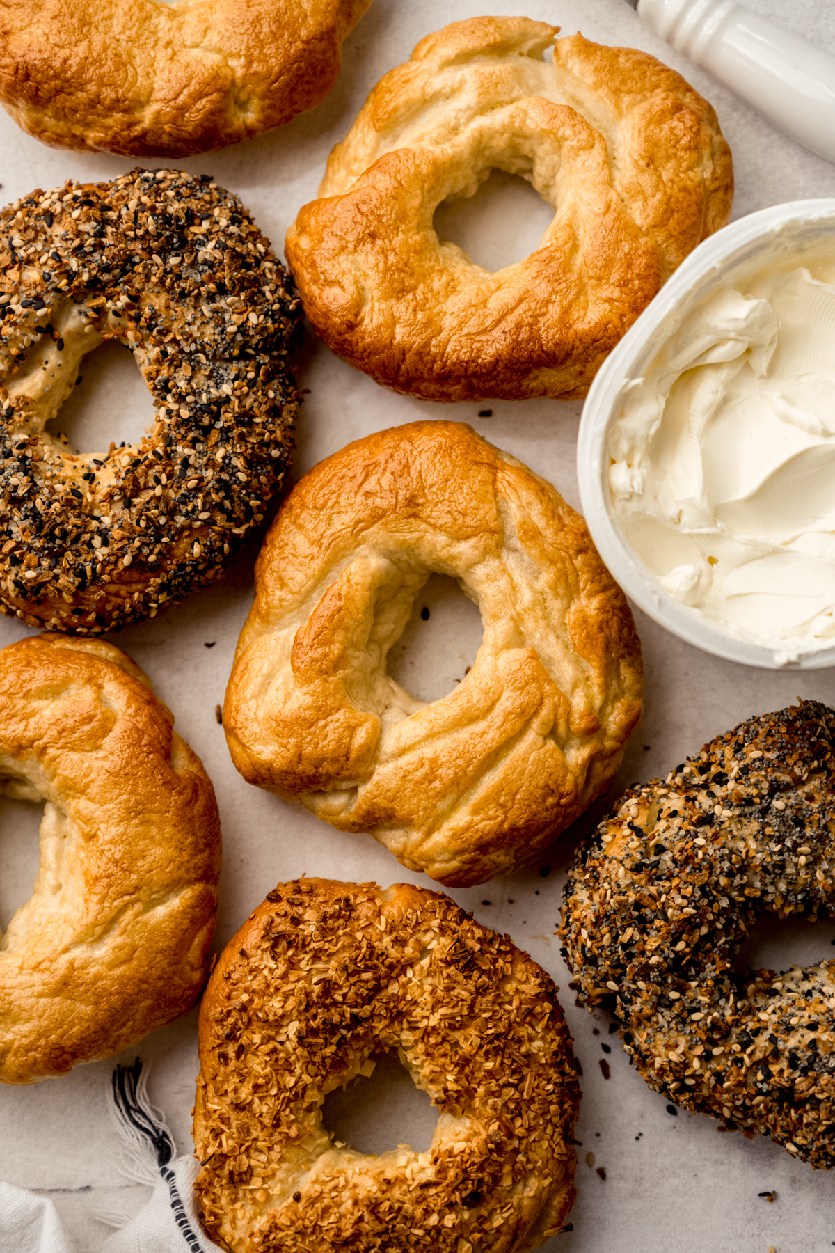 Aerial photo of homemade bagels on a surface with a tub of cream cheese.