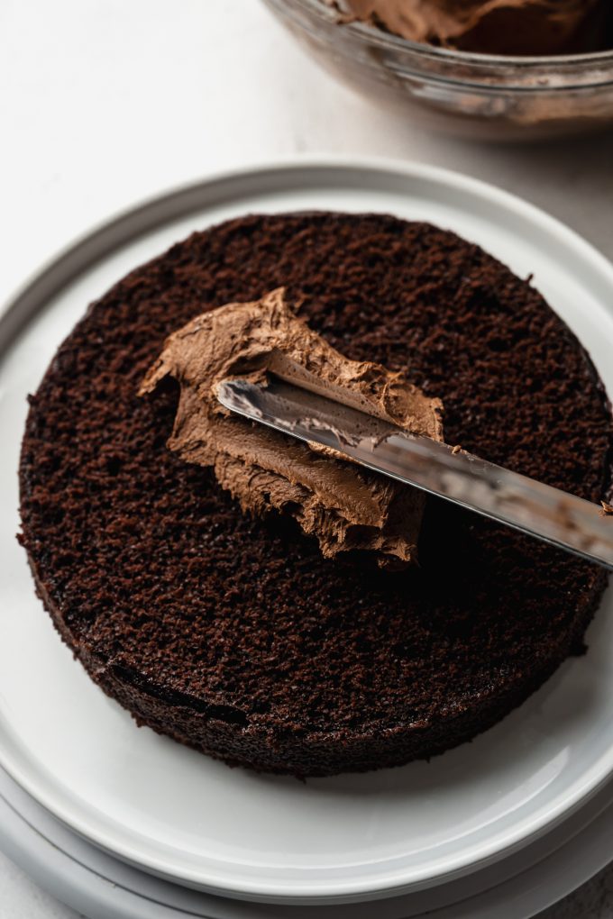 Someone is spreading chocolate frosting on a malt chocolate cake.