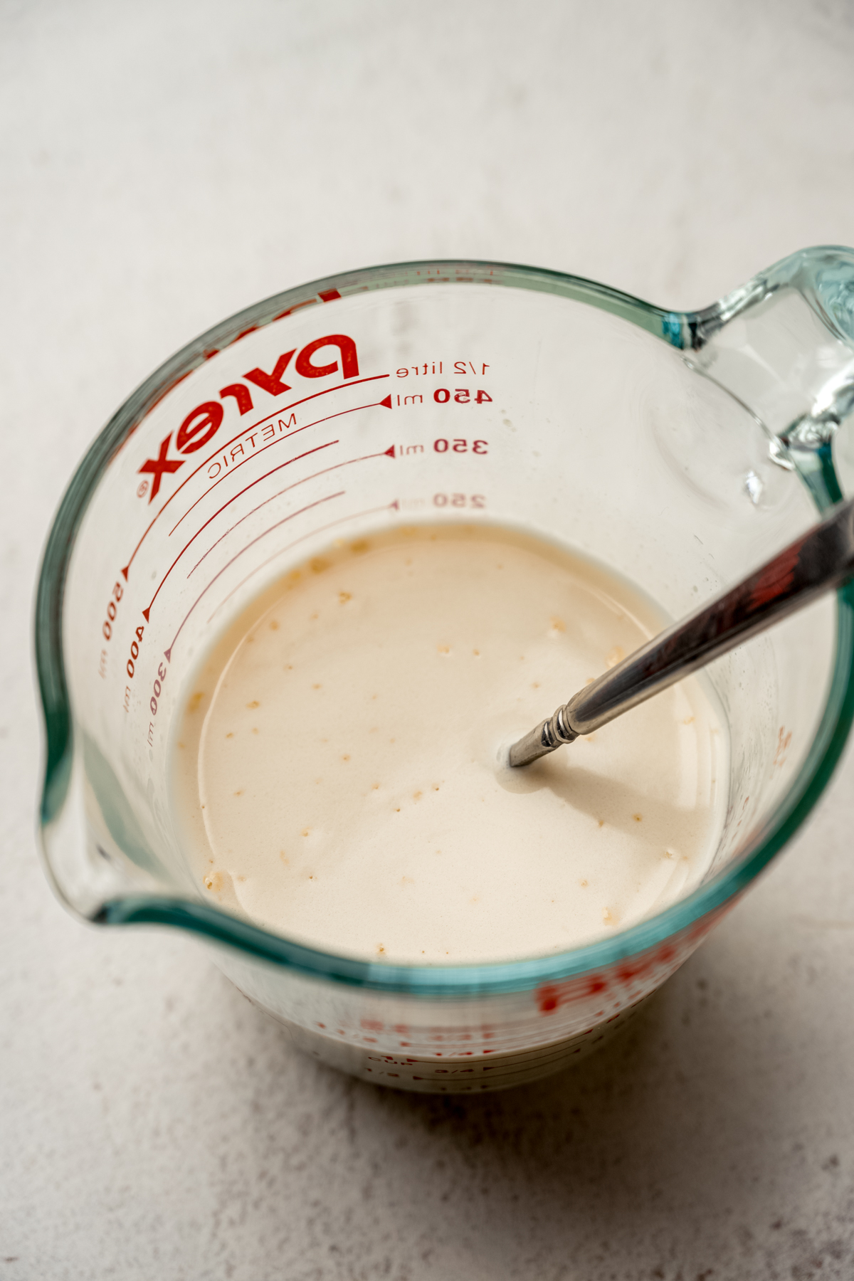 Malted milk in a large glass measuring cup with a spoon in it.