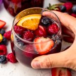Someone's hand around a glass of berry sangria.