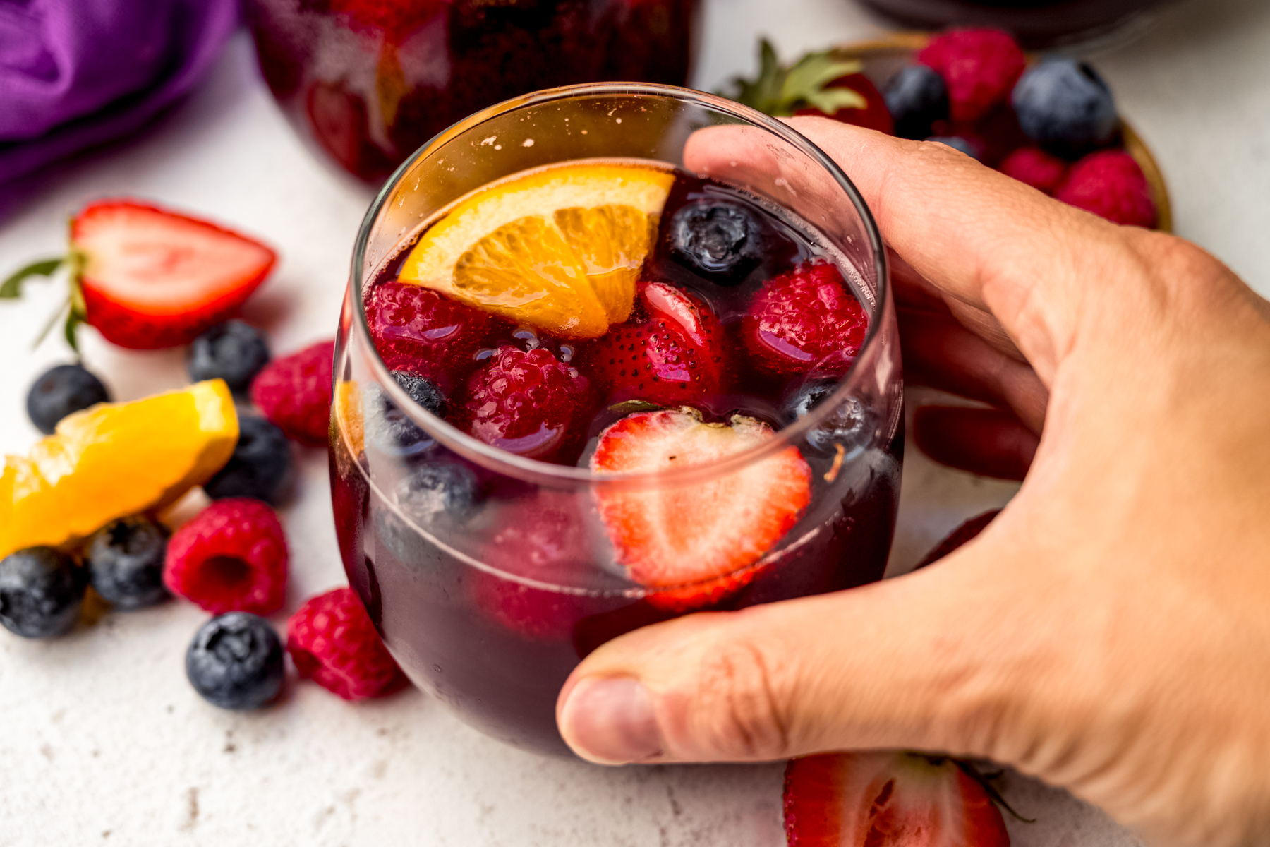 Someone's hand around a glass of berry sangria.