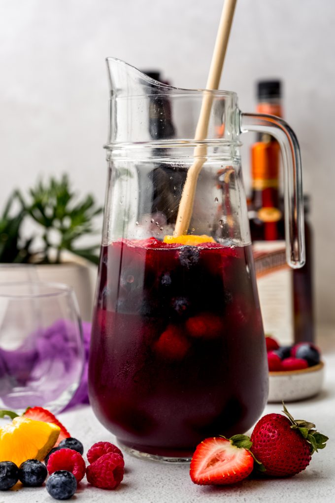 A glass pitcher of berry sangria with a wooden spoon in it.