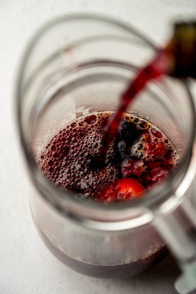 Aerial photo of someone pouring nonalcoholic wine into berry sangria in a pitcher.