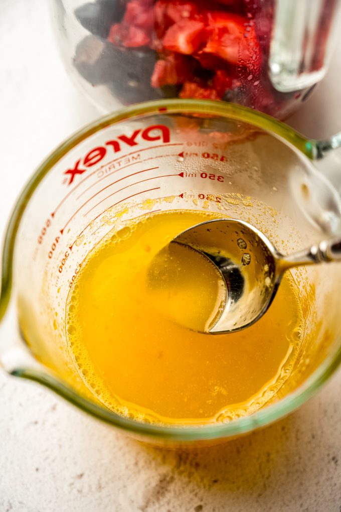 A measuring cup of orange syrup that someone is scooping up with a spoon.