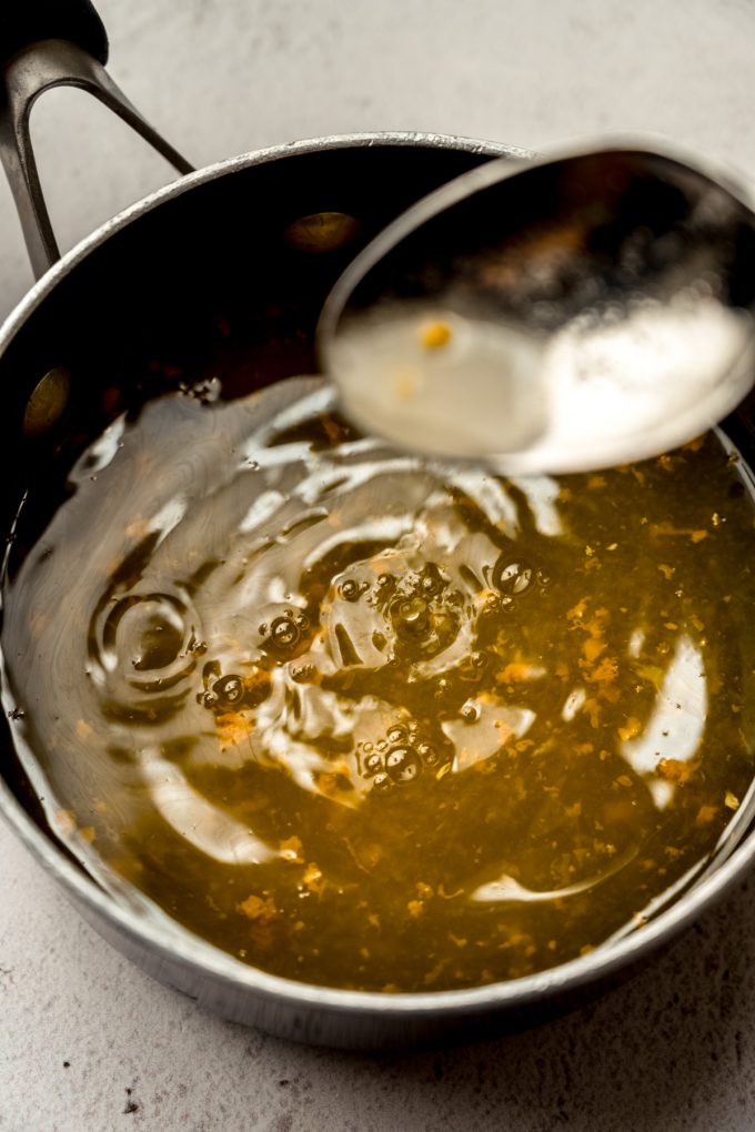 A saucepan of orange syrup that someone is scooping up with a spoon.
