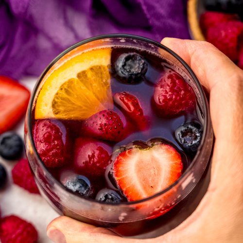 Aerial photo of someone's hand around a glass of berry sangria.