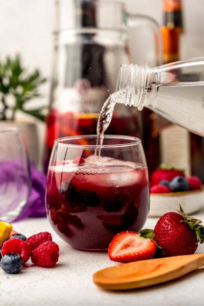 Someone is pouring seltzer water into a glass of berry sangria.