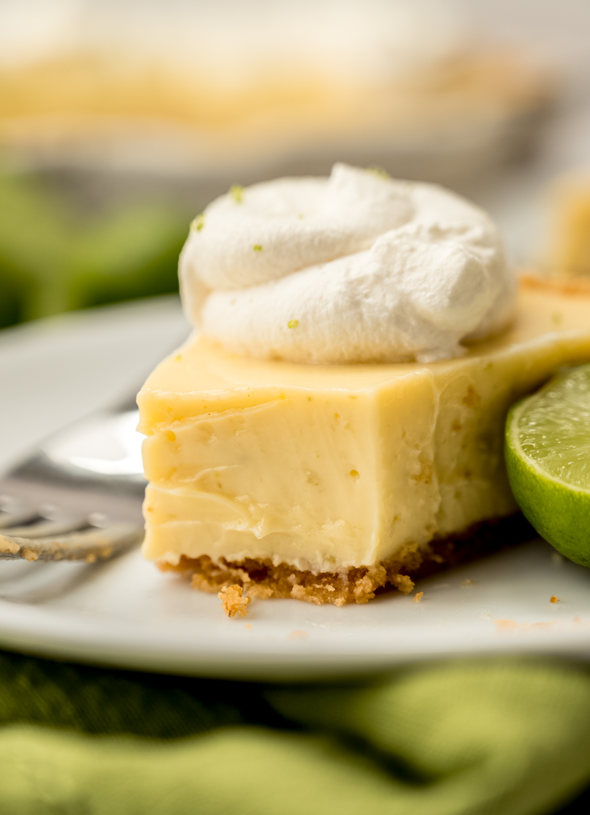 A photo of a slice of Key lime pie on a plate with a fork and a bite taken out of the slice.