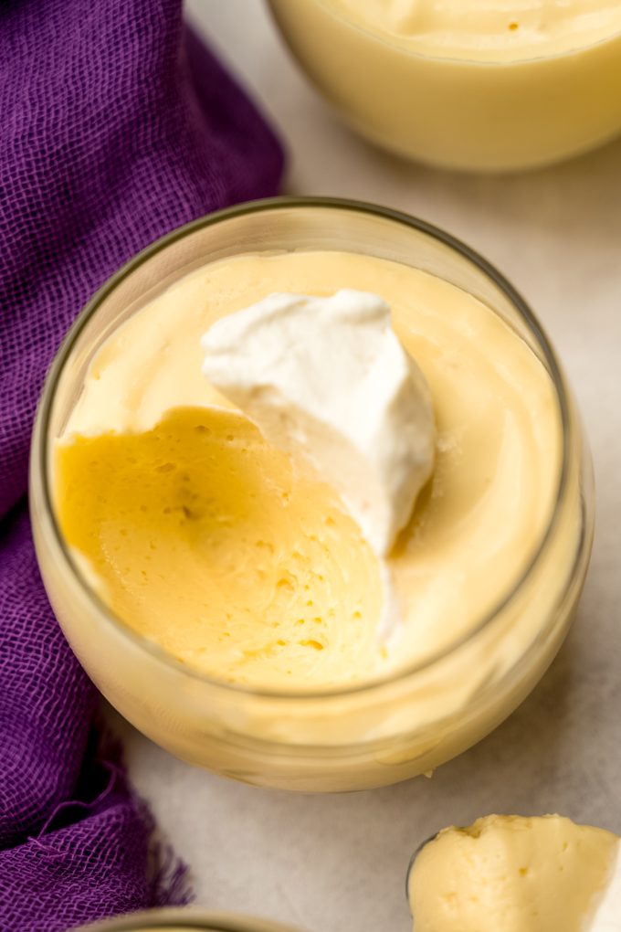 A dessert cup with passion fruit mousse with a spoonful taken out of it and the mousse has a dollop of whipped cream on top.