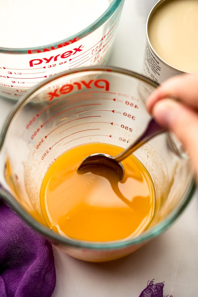 Someone is stirring passion fruit juice with a spoon in a glass measuring cup.