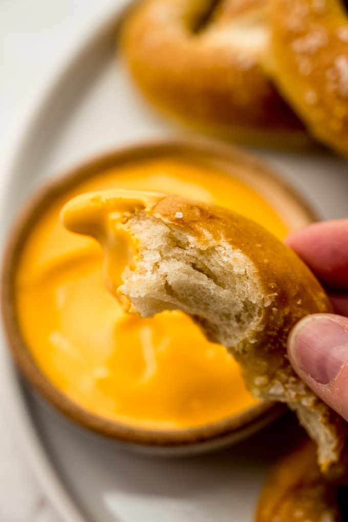Someone is holding a piece of homemade soft pretzel that's been dipped into cheese sauce.