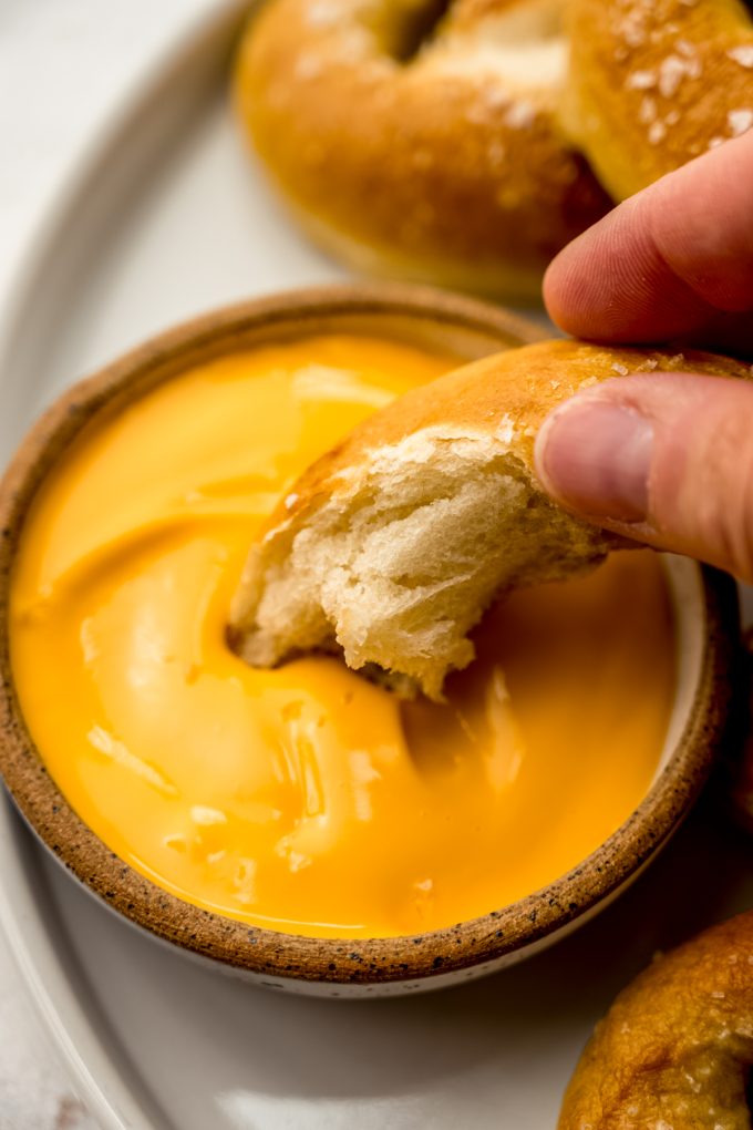 Someone is holding a piece of homemade soft pretzel that's been dipped into cheese sauce.