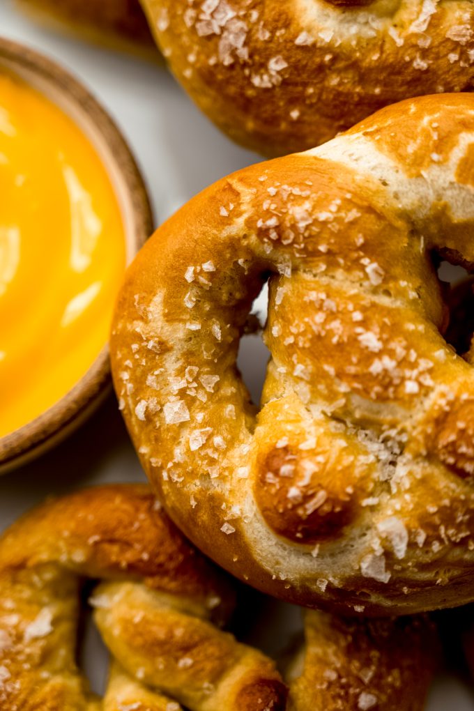 Someone is holding a soft pretzel near a bowl of cheese sauce.