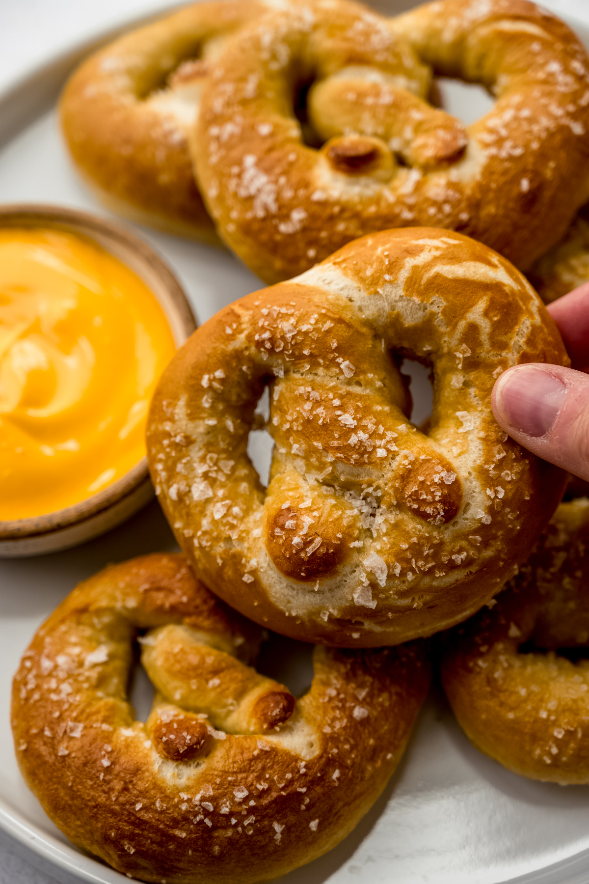 Someone is holding a soft pretzel near a bowl of cheese sauce.