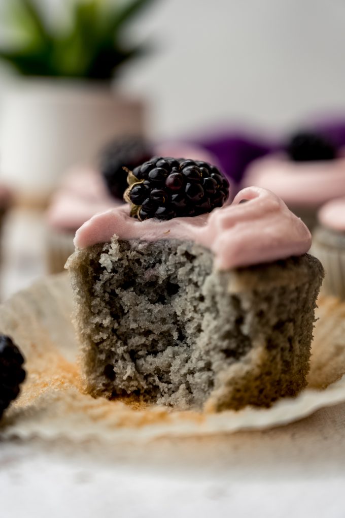 A blackberry cupcake on a surface with a bite taken out of it.
