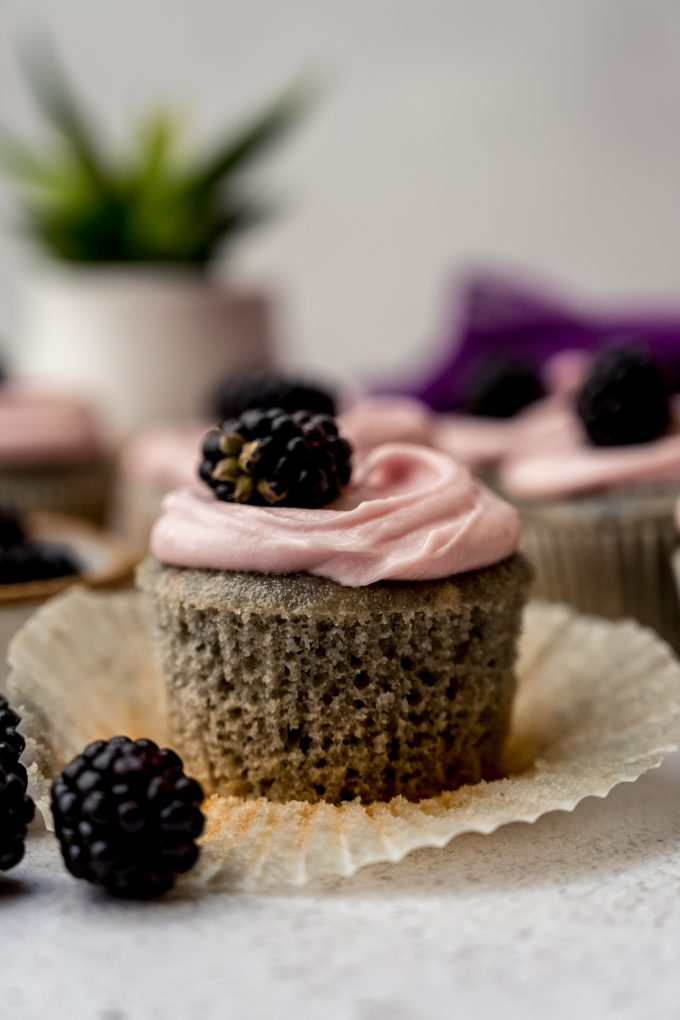 A blackberry cupcake on a surface with the wrapper taken off of it.