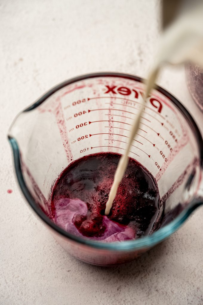 Someone is pouring milk into a measuring cup full of blackberry juice.