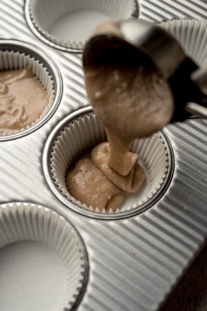 Someone is using an ice cream scoop with a trigger to put blackberry cupcake batter into the wells of a pan.
