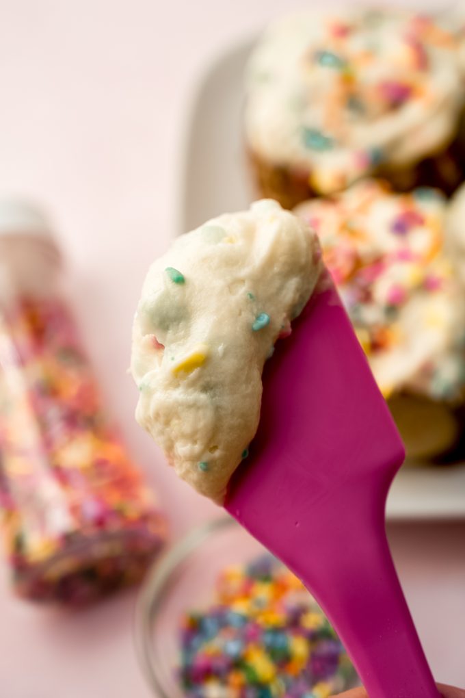 A pink spatula with rainbow chip frosting on it.