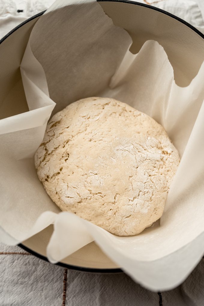 A boule of no knead bread dough in a parchment lined Dutch oven.