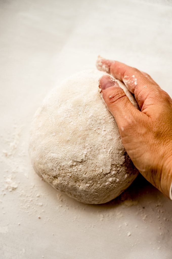 Someone is shaping a boule of no knead bread dough on a surface.