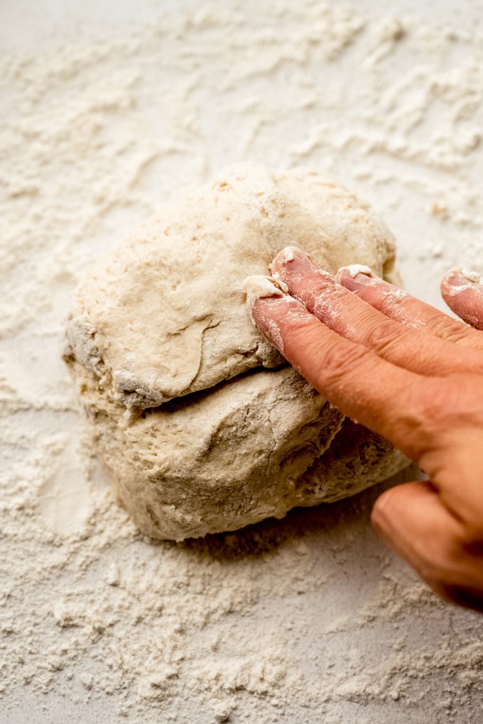 Someone is shaping a boule of no knead bread dough on a surface.