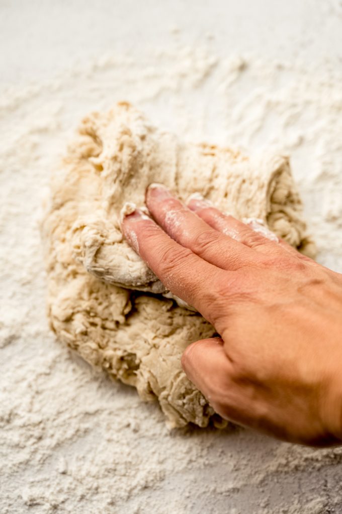 Someone is shaping a boule of no knead bread dough on a surface.