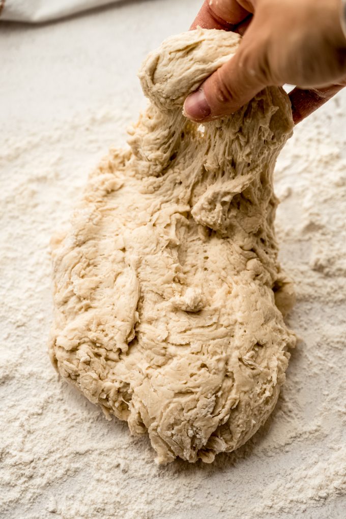 Someone is shaping a boule of no knead bread dough on a surface.