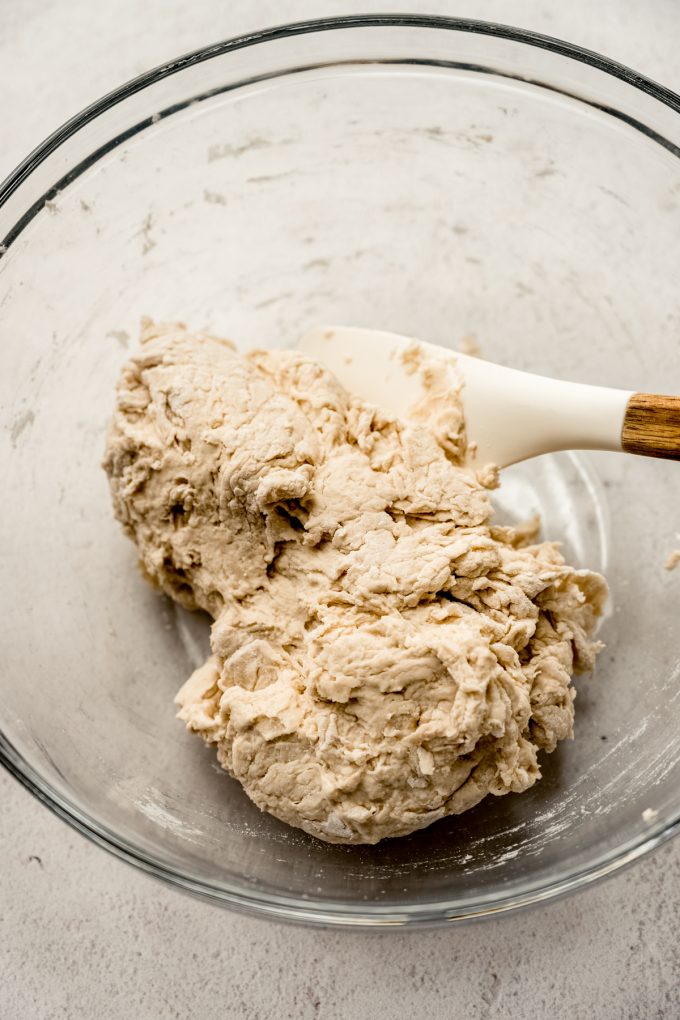 Shaggy bread dough in a glass bowl with a spatula.