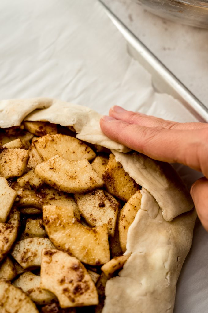 Someone is using their hand to fold up the sides of an apple galette.