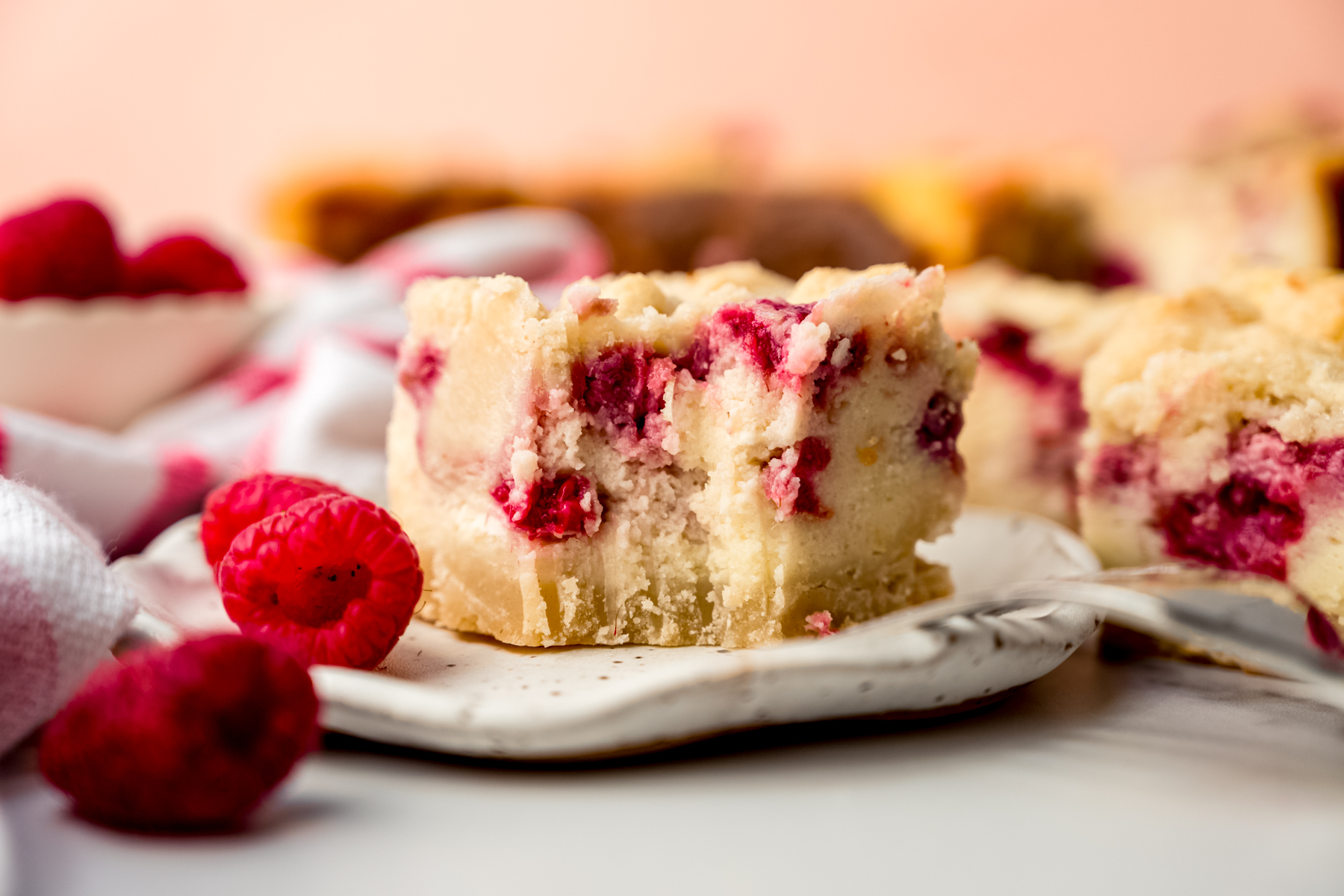A raspberry cheesecake bar on a plate and a bite has been taken out of it with a fork.