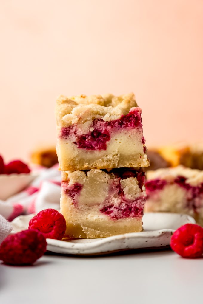 Two raspberry cheesecake bars stacked on top of each other on a plate.