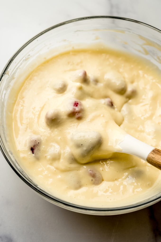 A bowl of raspberry cheesecake bar filling getting stirred with a spatula.
